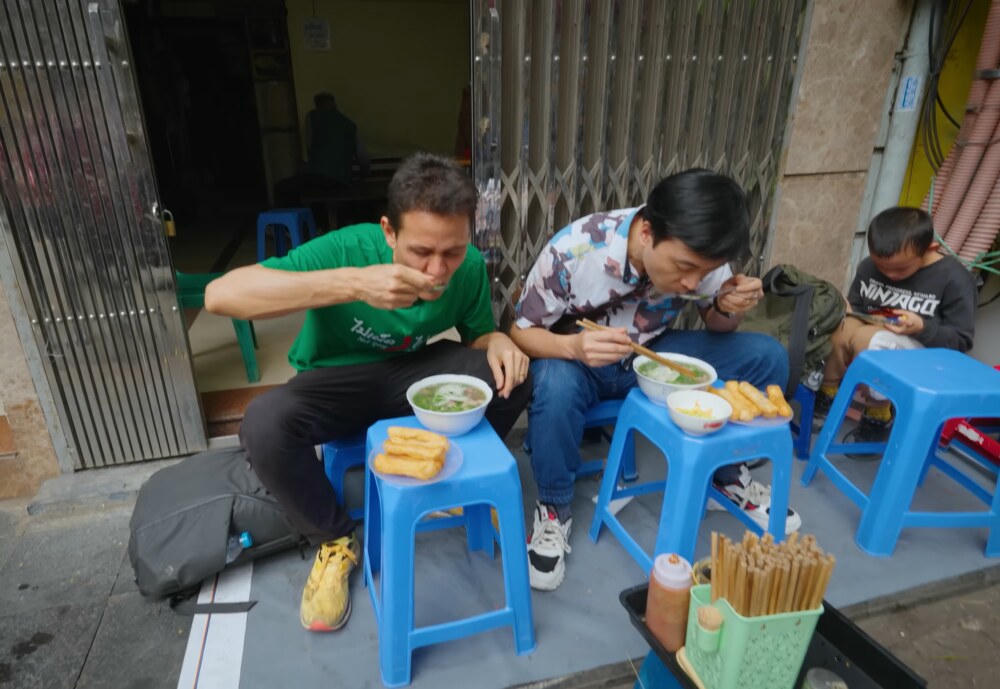 Mark Wiens ngồi ăn phở trên vỉa hè cùng người địa phương. Ảnh chụp màn hình